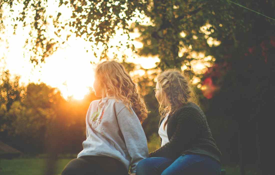 two women sitting near green tree during sunset